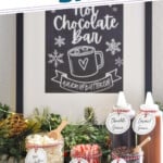 Pinterest graphic for Hot Chocolate Bar. Says says "the perfect Hot Chocolate Bar simplejoy.com" Image shows labeled jars of toppings for a Hot Chocolate Bar including mini marshmallows, peppermint sticks, chocolate chips, kosher salt, toffee bits, peppermint chips, chocolate sauce, and caramel sauce.