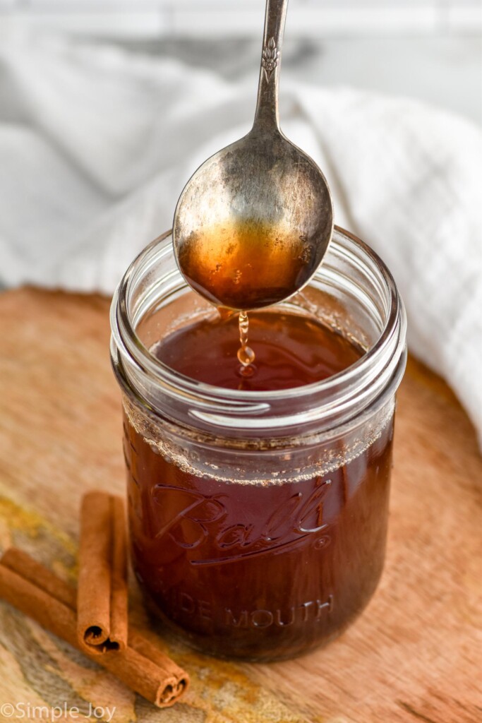 a spoon pouring cinnamon simple syrup into a mason jar