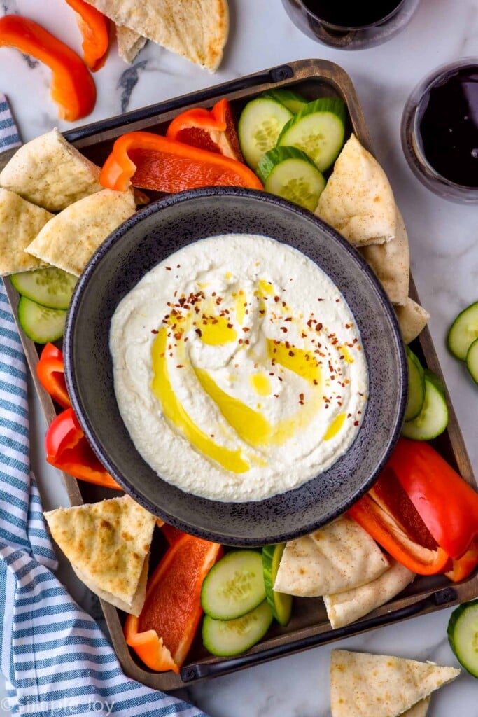 overhead of bowl of Whipped Feta Dip topped with olive oil and crushed red pepper flakes surrounded by cucumber slices, red pepper slices, and pita bread for serving.