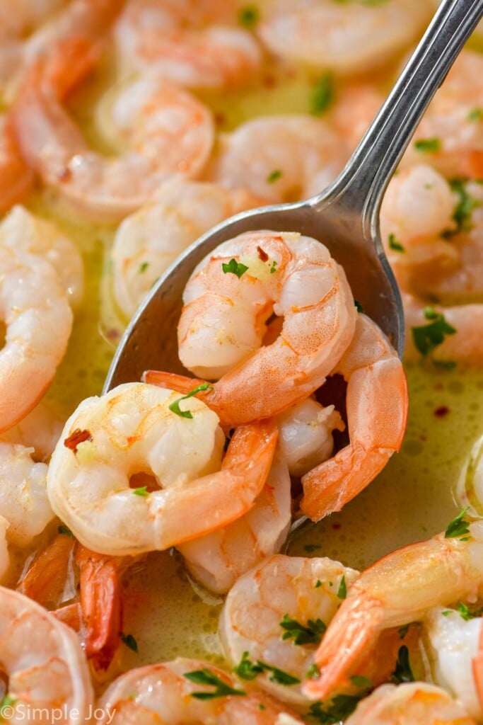 spoon holding Garlic butter shrimp in a skillet of Garlic butter shrimp