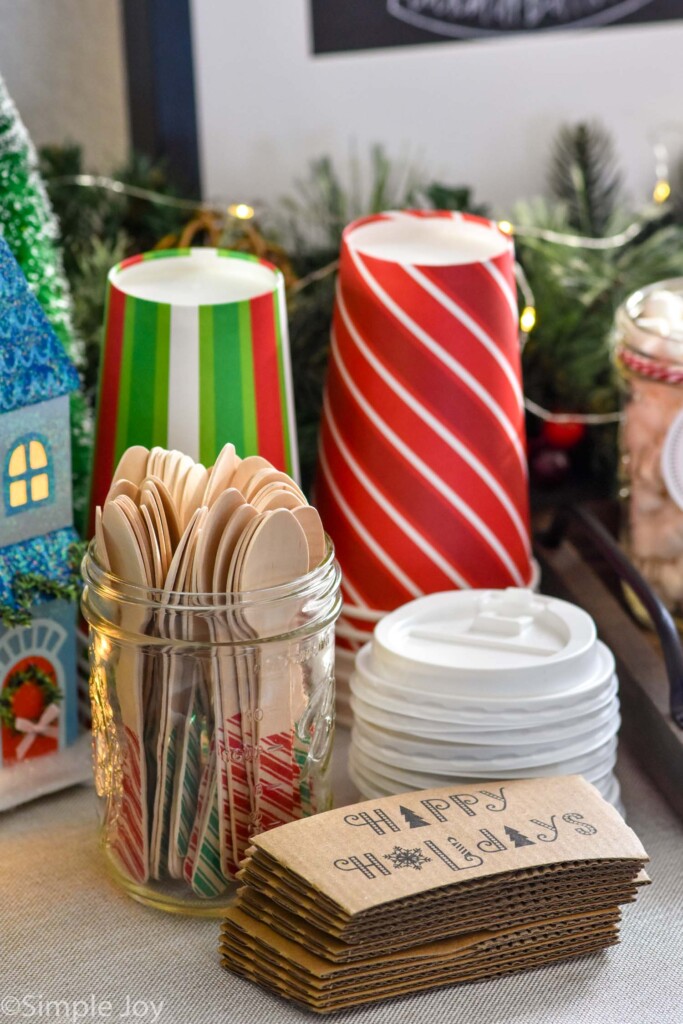 Cups, lids, and jar of small wooden spoons to make a Hot Chocolate Bar