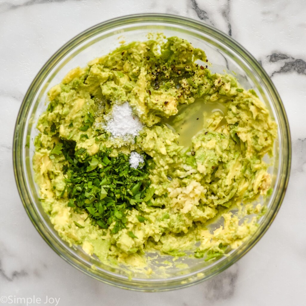 Overhead view of glass bowl of avocado and seasonings for Seven layer dip recipe.