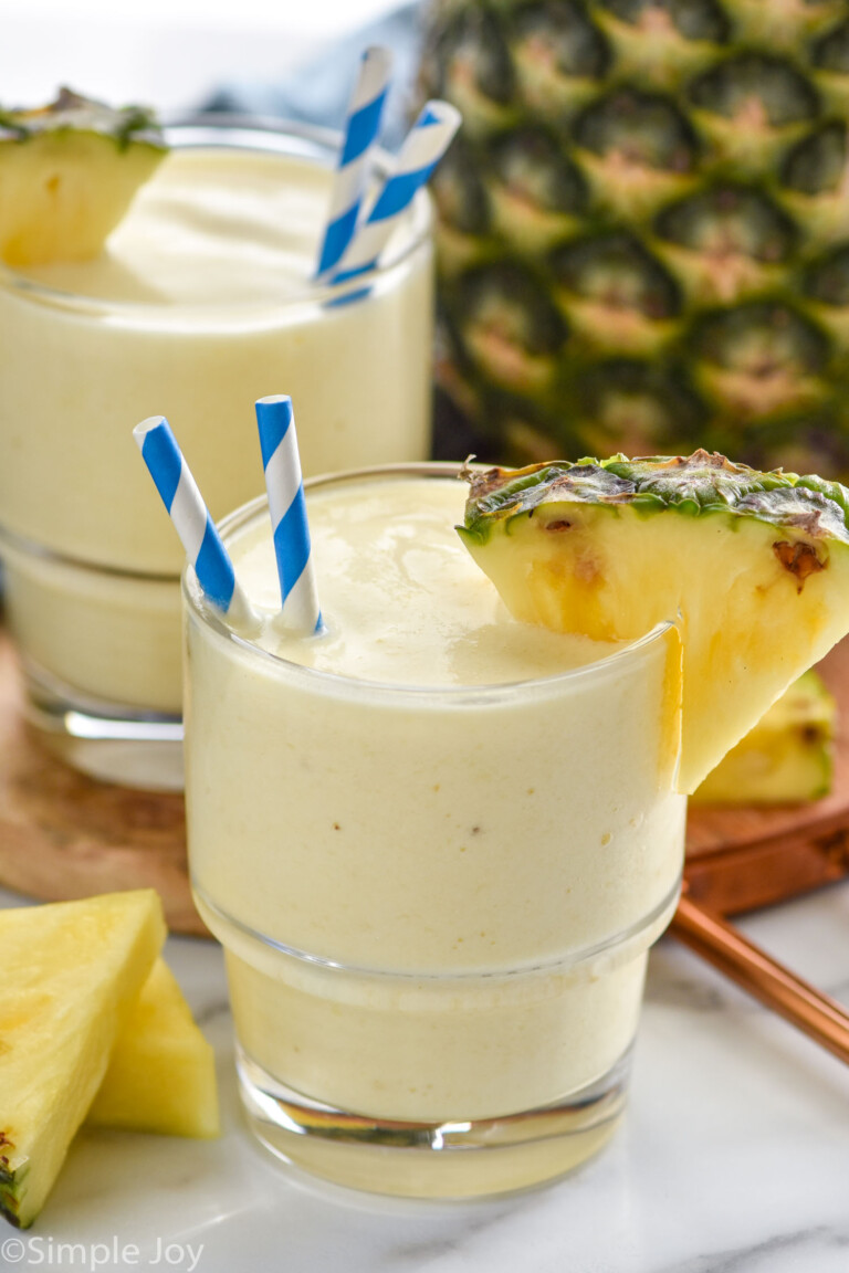 Two glasses of Pineapple Smoothie with straws and fresh pineapple wedge on the rim