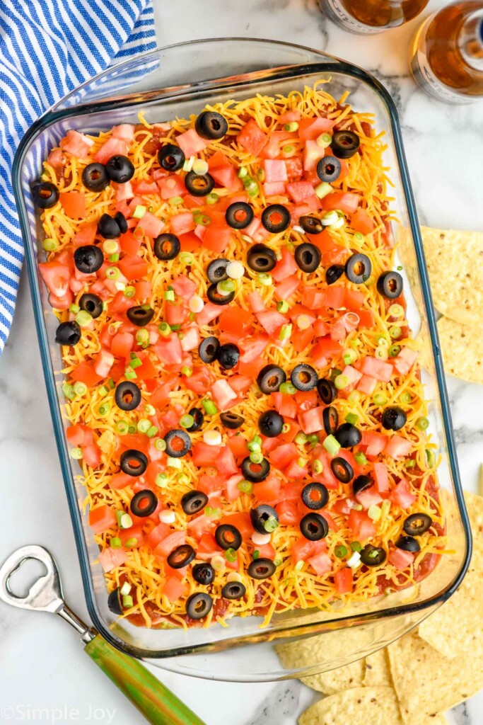 Overhead view of glass dish of Seven layer dip with chips and bottle opener beside.