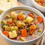 Bowl of Vegetable Beef Soup with spoons and piece of bread sitting beside