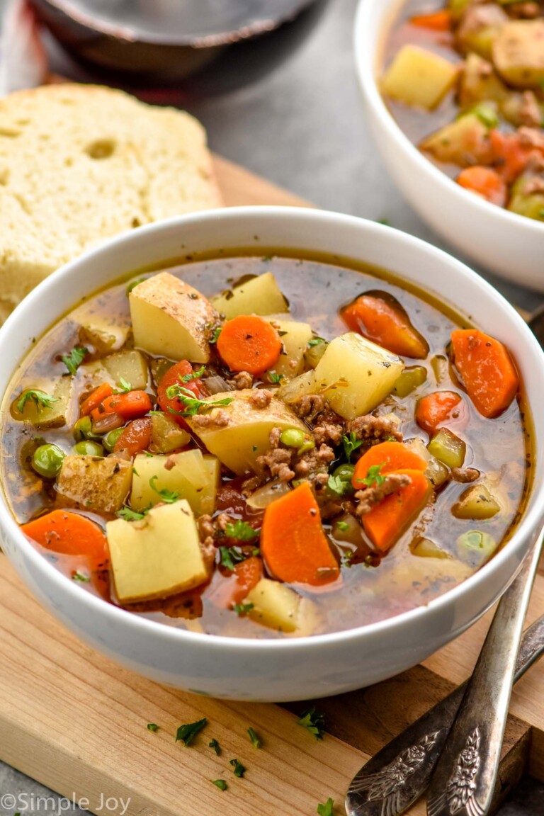 Bowl of Vegetable Beef Soup with spoons and piece of bread sitting beside