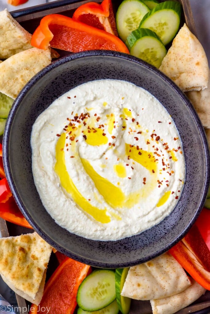 overhead of bowl of Whipped Feta Dip topped with olive oil and red pepper flakes. Cucumber slices, red pepper slices, and pita bread surrounding