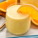 Pinterest graphic for orange smoothie recipe. Image shows glasses of orange smoothie with orange slices on the rim. Orange and orange slices beside for garnish. Text says, "orange smoothie simplejoy.com."