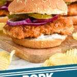 Pinterest graphic for Pork Tenderloin Sandwich recipe. Image shows side view of a Pork Tenderloin Sandwich garnished with onion and pickles, chips beside. Text says, "Pork Tenderloin Sandwich simplejoy.com"