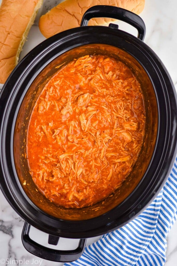 Overhead view of a slow cooker with Slow Cooker Buffalo Chicken recipe, buns beside