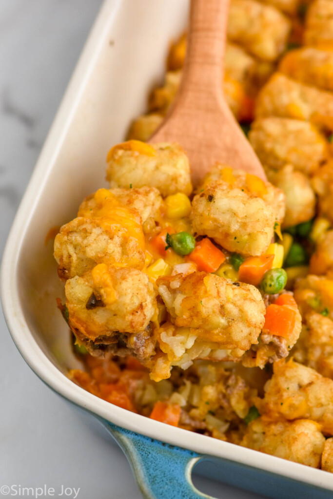 Wooden spoon holding tater tot casserole out of baking dish