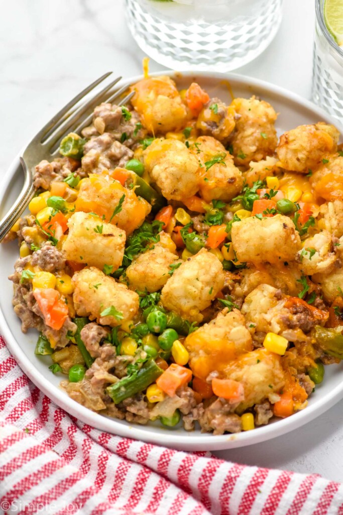 plate of tater tot casserole topped with fresh parsley and fork sitting beside