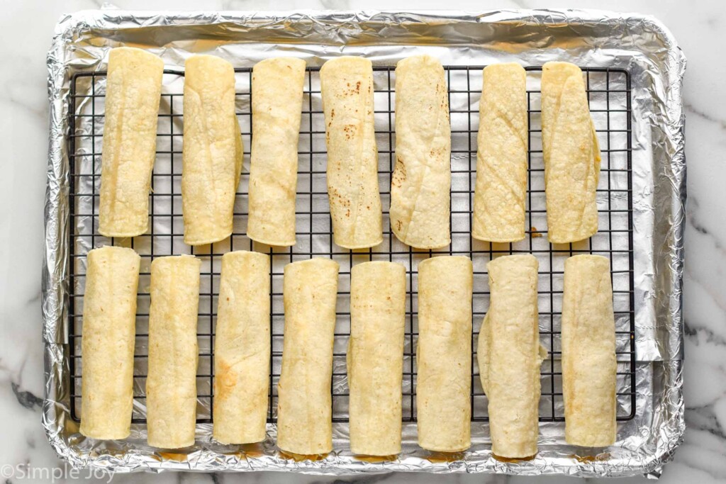 Overhead view of a baking sheet with a wire rack with Chicken Taquitos ready for baking.