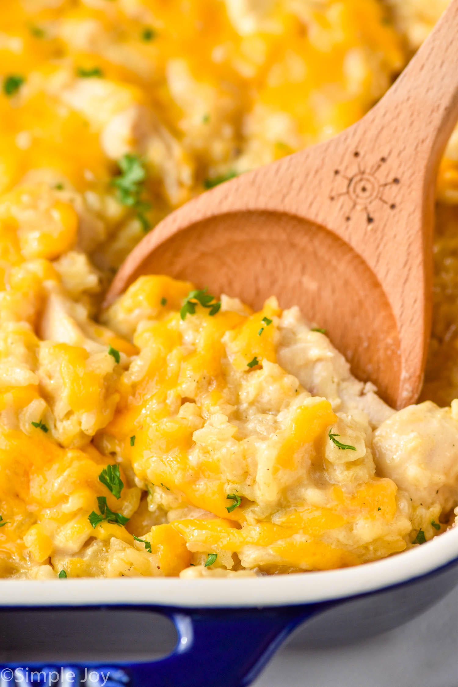 Close up of a wooden spoon in a casserole dish of Chicken and Rice Casserole recipe.