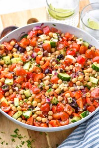 Bowl of chick pea salad garnished with parsley. Drinks beside.