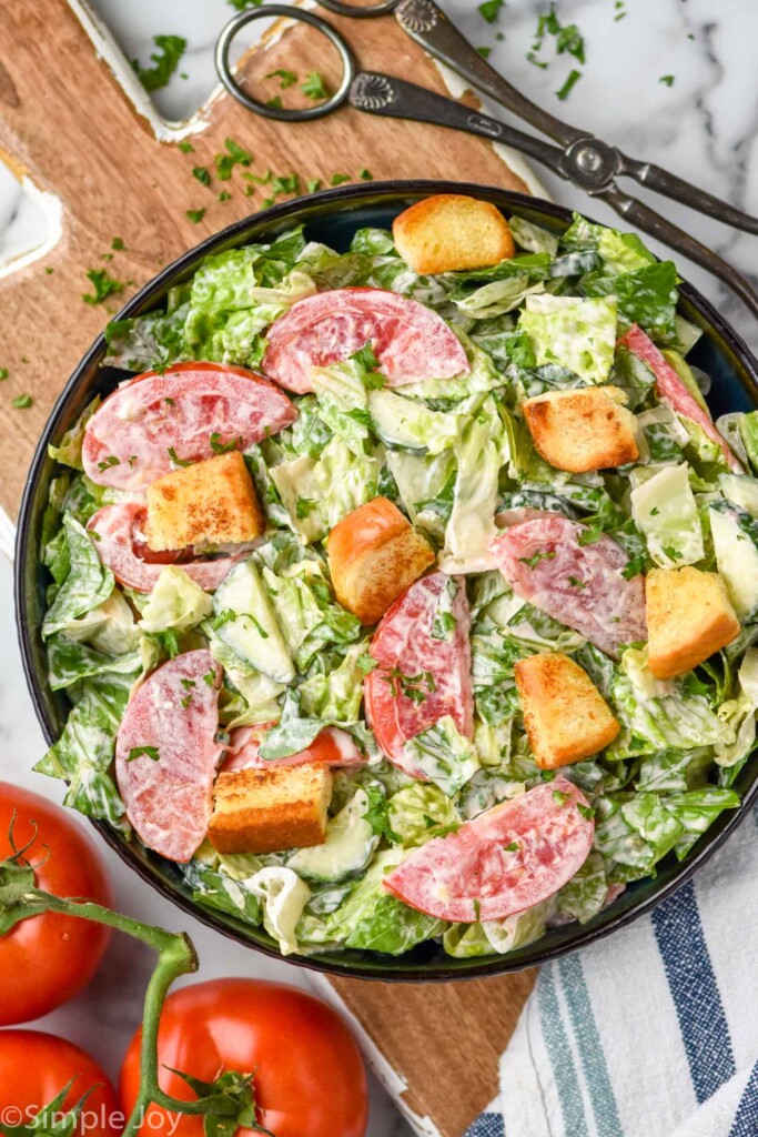 Overhead view of a salad with Thousand Island Dressing, tomatoes, and croutons. Salad tongs and whole tomatoes beside.