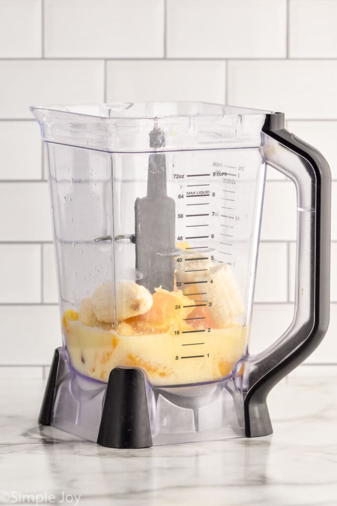 Side view of a blender pitcher with ingredients for orange smoothie recipe.