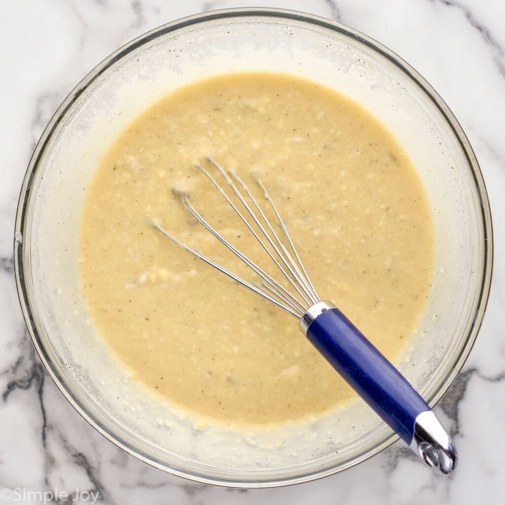 Overhead view of a glass mixing bowl of ingredients with a whisk for Chicken and Rice Casserole recipe