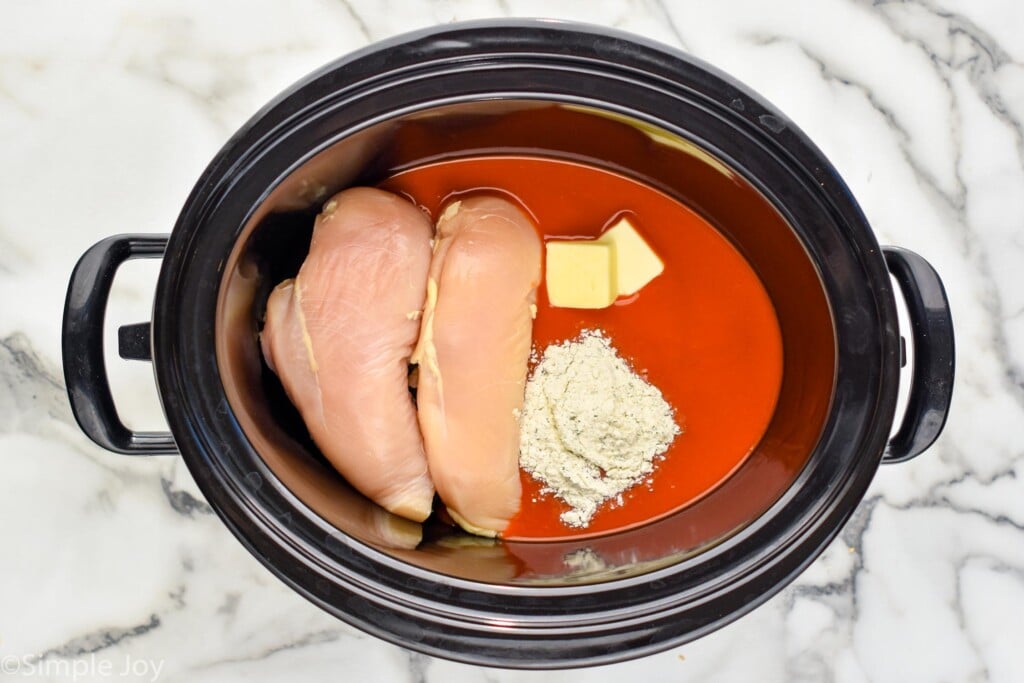 Overhead view of a crock pot of ingredients for Slow Cooker Buffalo Chicken recipe.