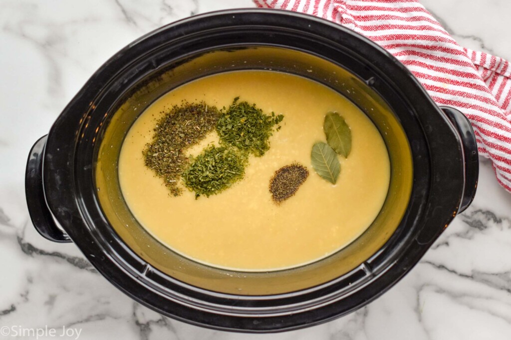 Overhead view of crock pot with broth and seasonings for Crockpot Chicken and Dumplings recipe.