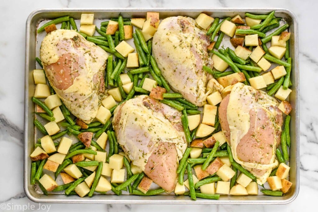 raw chicken that has been marinated, potatoes, and green beans on a sheet pan