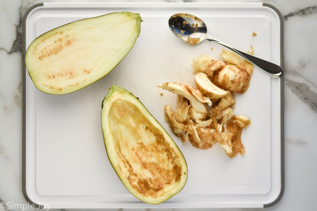 overhead of eggplant on a cutting board with scooped out eggplant and spoon sitting beside