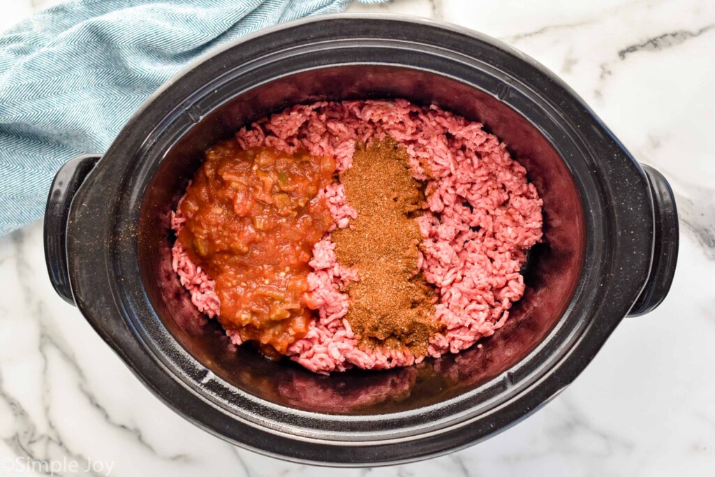 Overhead view of a crock pot with hamburger and seasonings for Slow Cooker Taco Meat recipe.