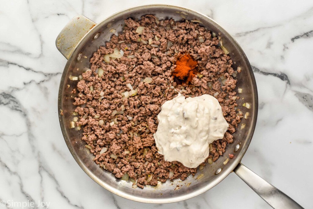 overhead of skillet of ground beef with onion and other tater tot casserole ingredients