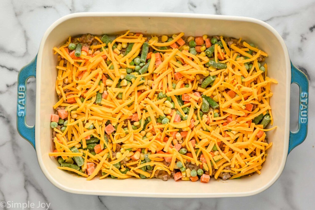 Overhead of baking dish of tater tot casserole ingredients topped with shredded cheddar cheese