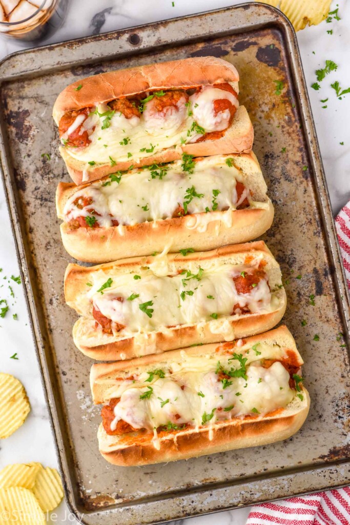 Overhead view of baking sheet with meatball subs. Potato chips beside.