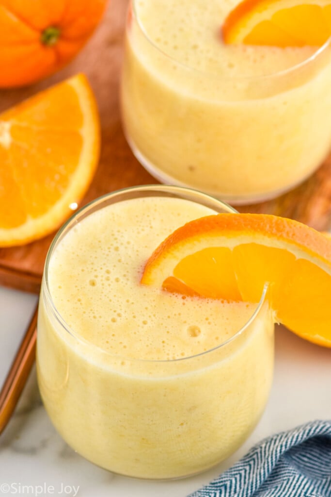 Close up view of glasses of orange smoothies with orange slices on the rim. Orange slices beside for garnish.