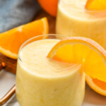 glasses of orange smoothie with orange slices on the rip. Orange and orange slices beside for garnish.