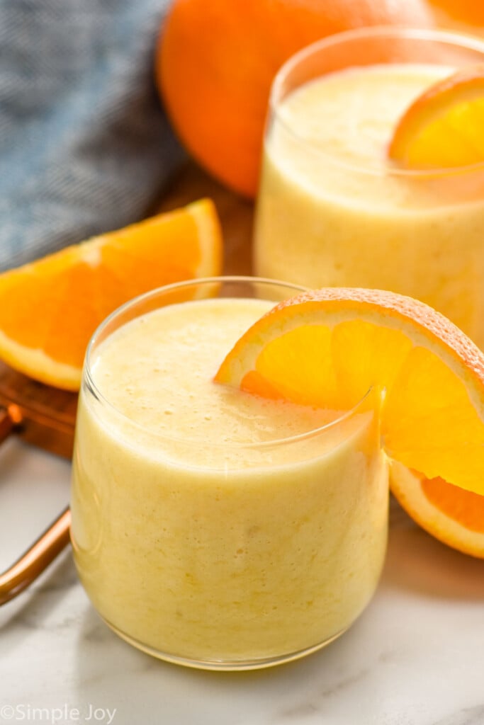 glasses of orange smoothie with orange slices on the rip. Orange and orange slices beside for garnish.