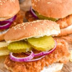 Pork Tenderloin Sandwich garnished with pickles and onions, chips beside