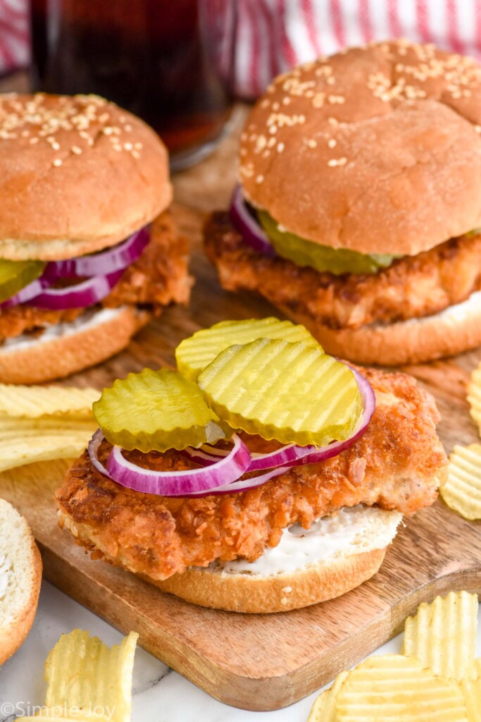 Pork Tenderloin Sandwich with pickles and onions, top bun missing. Chips beside.