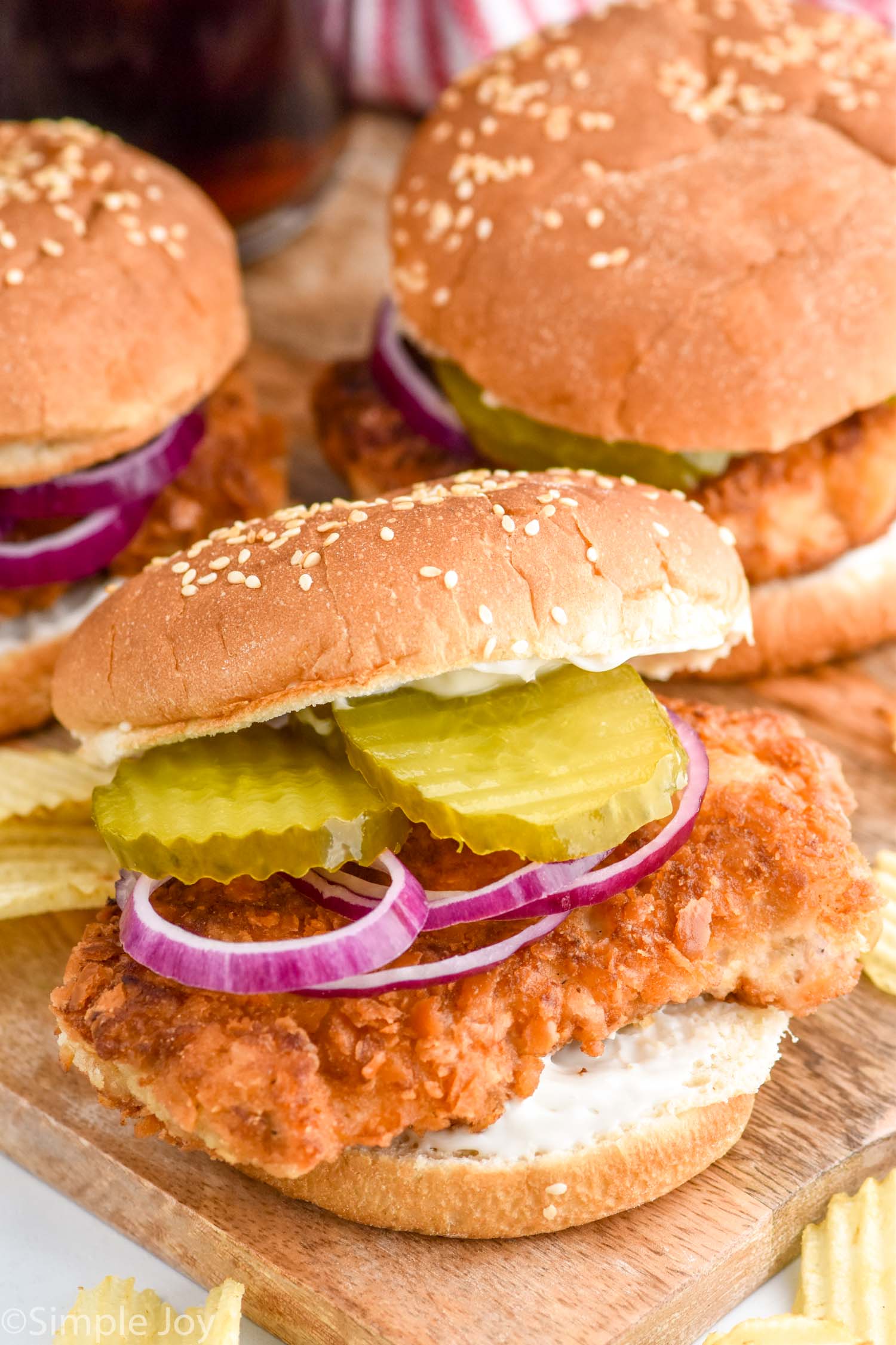 Pork Tenderloin Sandwich garnished with pickles and onions, chips beside