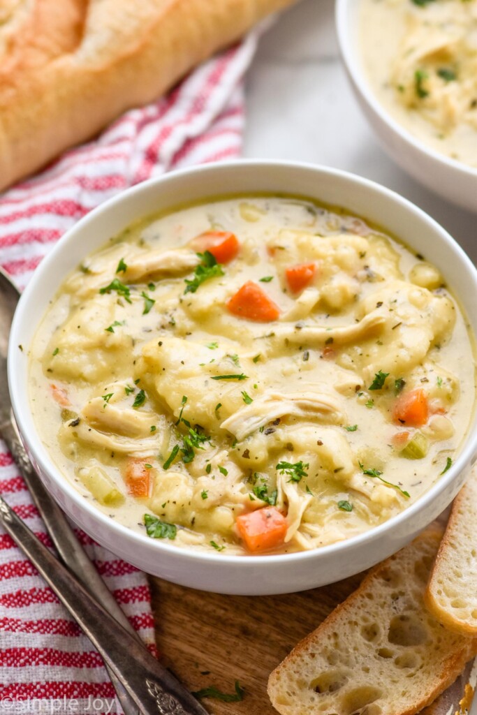 Bowl of Crockpot Chicken and Dumplings with bread and spoons beside