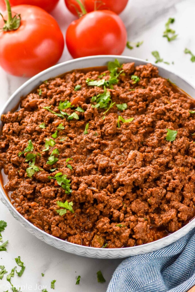 Bowl of Slow Cooker Taco Meat garnished with cilantro, tomatoes beside