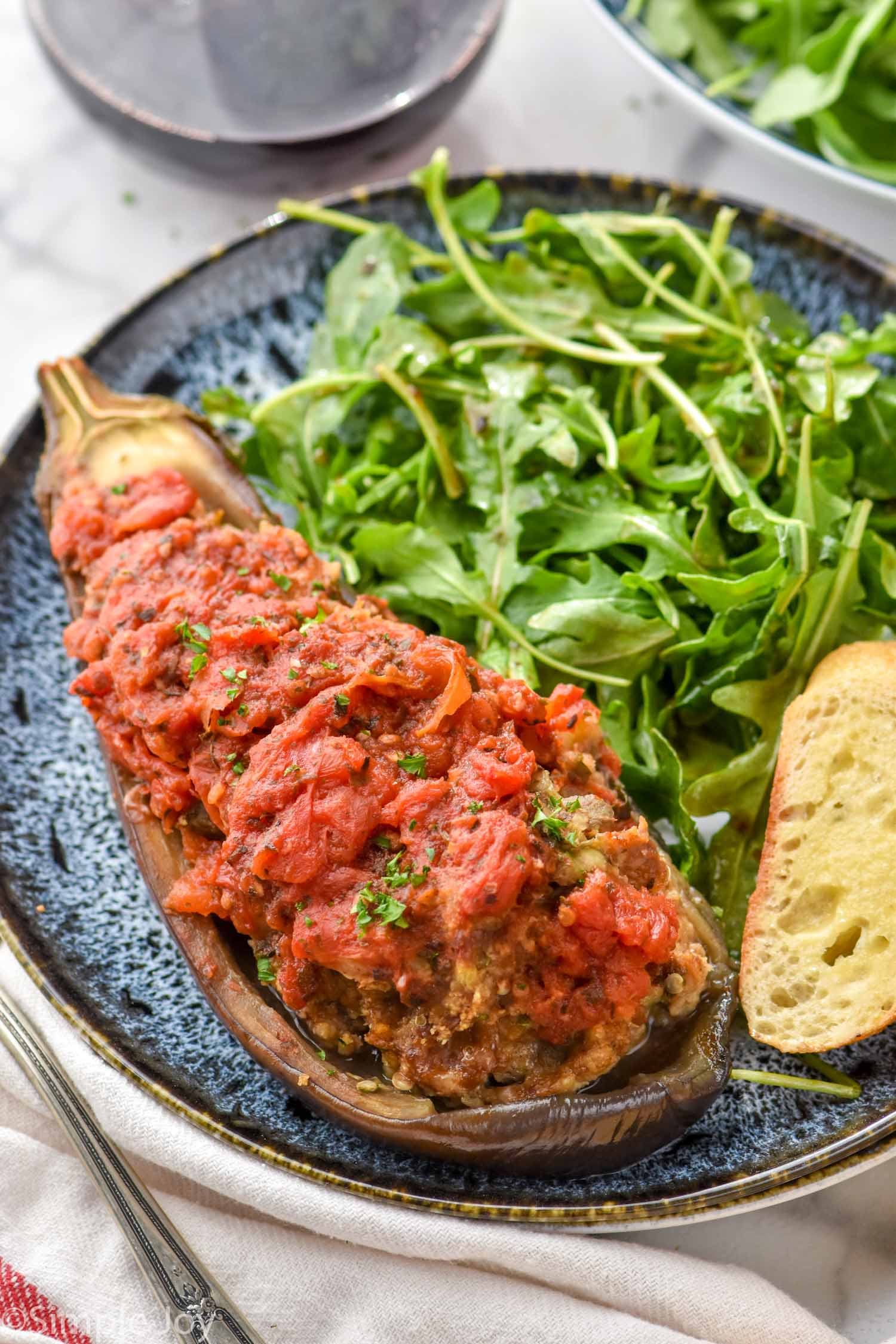 Plate of Stuffed Eggplant topped with fresh parsley with arugula salad and piece of bread beside