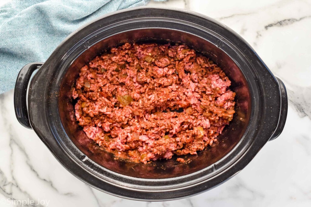 Overhead view of hamburger and seasonings in slow cooker for Slow Cooker Taco Meat recipe