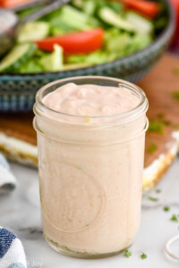 Jar of Thousand Island Dressing recipe with bowl of salad behind.