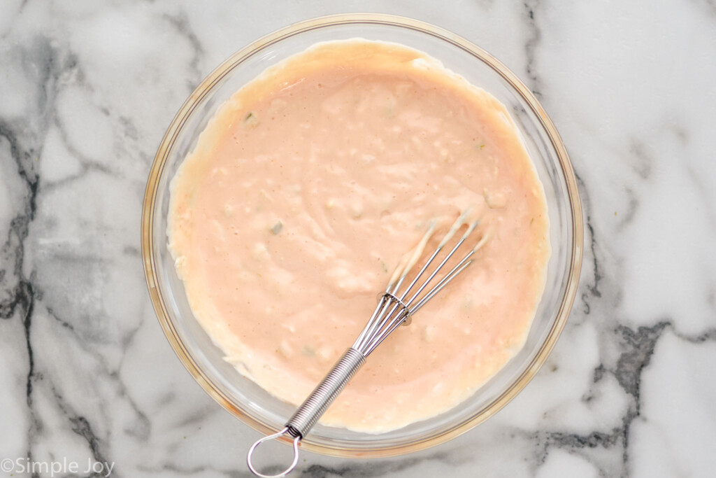 Overhead view of a glass mixing bowl of Thousand Island Dressing recipe with a whisk for combining.