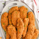 Pinterest graphic for Baked Chicken Tenders. Says "the best chicken tenders simplejoy.com" Image shows overhead of a platter of Baked Chicken Tenders with a small cup of sauce for dipping. French fries sitting beside plate.