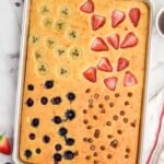 Overhead view of Sheet Pan Pancakes garnished with bananas, strawberries, blueberries, and chocolate chips in quadrants. Cup of coffee and berries beside.