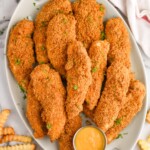 Overhead of platter of Baked Chicken Tenders with small cup of dipping sauce and french fries sitting beside