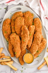 Overhead of platter of Baked Chicken Tenders with small cup of dipping sauce and french fries sitting beside