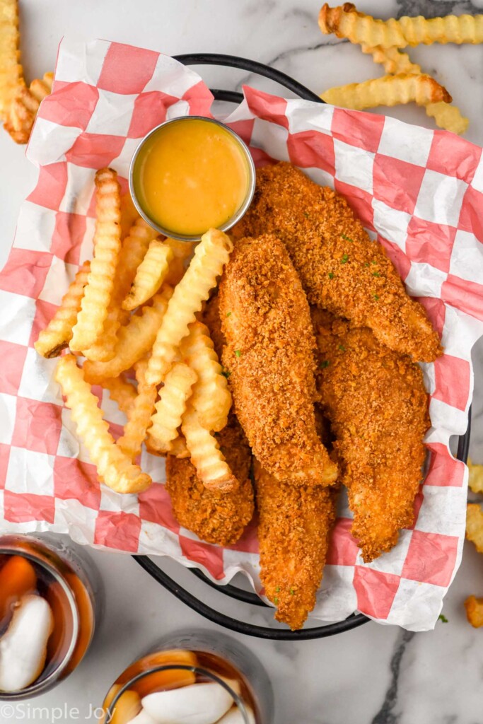 overhead of basket of Baked Chicken Tenders, french fries, and small cup of sauce for dipping.