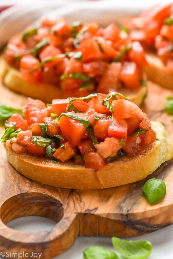 Bruschetta on wooden serving board, with basil leaves beside.