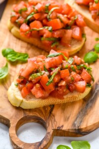 Bruschetta served on a wooden board garnished with basil leaves