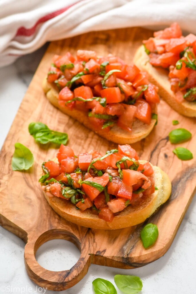 Wooden board with Bruschetta on it, basil leaves beside.